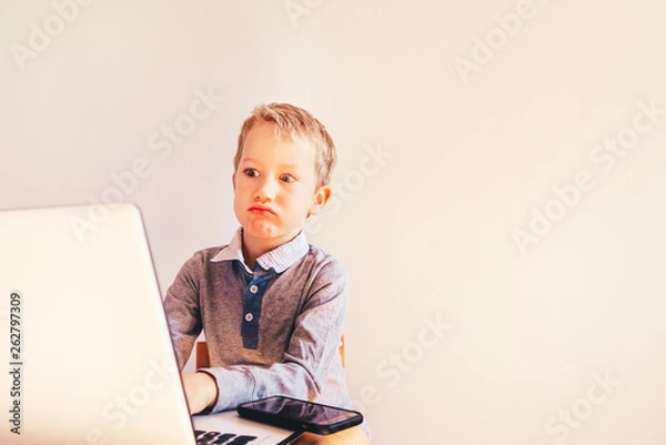 Fototapeta Child 5 years old working on a laptop with an angry face when business failing, humor image.