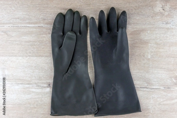 Fototapeta black protective rubber gloves for working with caustic substances, on a light wooden background, short focus