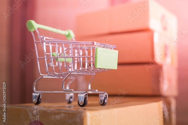 Obraz mini green shopping cart with cardboard boxes in background