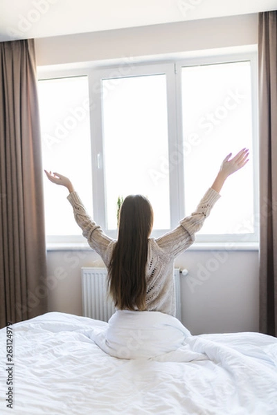Fototapeta Rear view of woman stretching in bed after wake up in morning