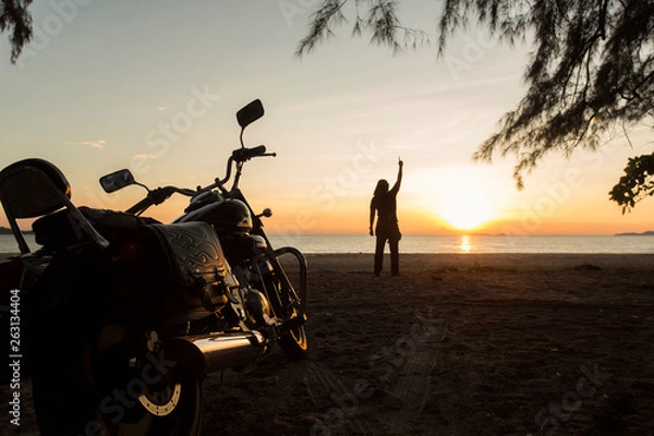 Fototapeta The young man stood on the beach. With a motorcycle parked He raised his hand to the sky. As if he had accomplished something