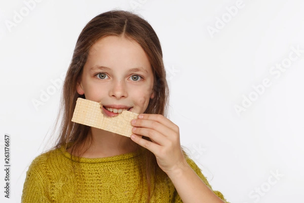 Obraz Portrait of a beautiful 8 year old girl in a sweater and with a wafer in her hand. White background