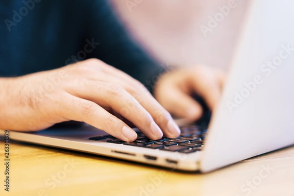 Fototapeta Sideview of man using laptop on desktop