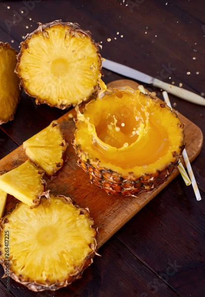 Fototapeta Splash fresh fruit juice with exotic pineapple on a wooden brown table. A composition made of ananas. Top wiev. 