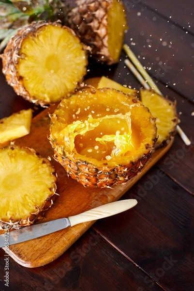 Fototapeta Splash fresh fruit juice with exotic pineapple on a wooden brown table. A composition made of ananas. Top wiev. 