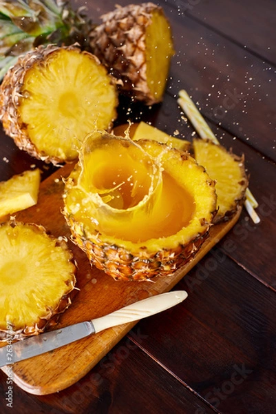 Fototapeta Splash fresh fruit juice with exotic pineapple on a wooden brown table. A composition made of ananas. Top wiev. 