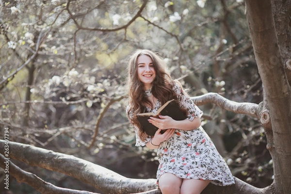 Fototapeta beautiful young woman reading a retro book in a garden with blooming trees