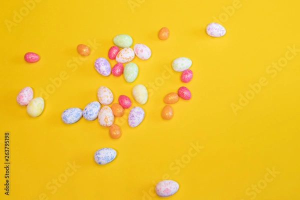 Fototapeta A lot of colorful Easter eggs on a yellow background. Top view, minimal Easter concept. Happy Easter card  with free, empty space.