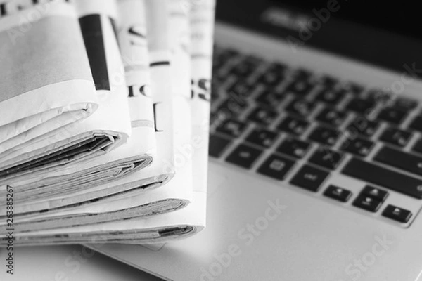 Obraz Newspapers and laptop. Pile of daily papers with news on the computer. Pages with headlines, articles folded and stacked on keypad of electronic device. Modern gadget and old journals, focus on paper