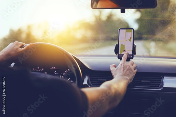 Obraz Kierowca za pomocą nawigacji GPS w telefonie komórkowym podczas jazdy samochodem o zachodzie słońca