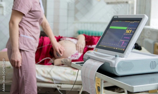 Fototapeta Kobieta w ciąży z elektrokardiografem sprawdza swoje dziecko. Monitorowanie pracy serca płodu. Diagnostyka, opieka zdrowotna, usługi medyczne