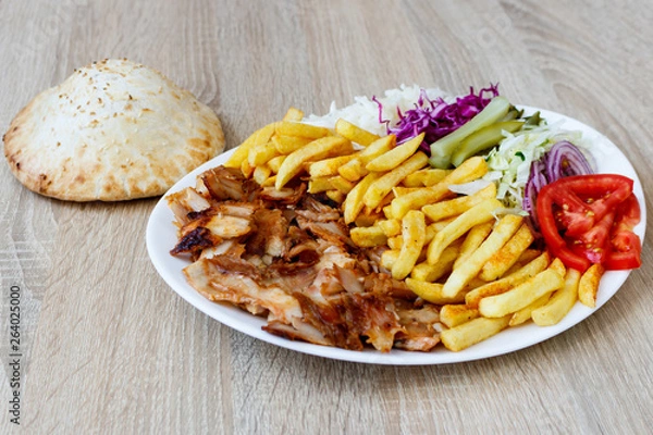 Obraz Chiken Doner Kebab on the plate with bread, french fries, tomatoes, onion, pickles and salad on a wooden background. Grilled chicken meat with vegetables.