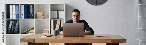Obraz Young man working with computer, phone and tablet at the table while drinking coffee