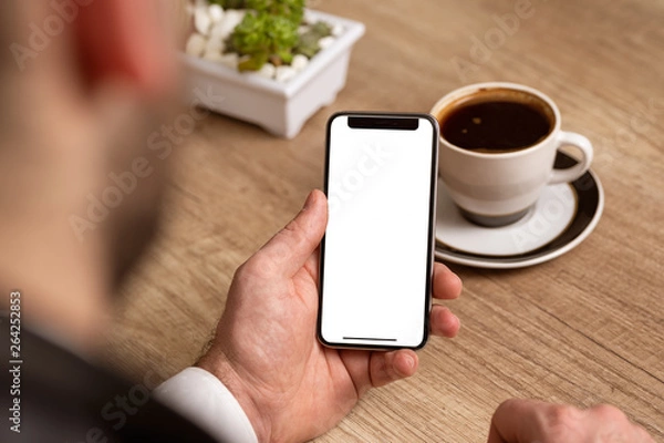 Fototapeta Business man holding phone with white empty screen at work place