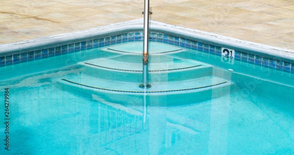 Fototapeta three curved steps going into a swimming pool with a rusted metal hand rail