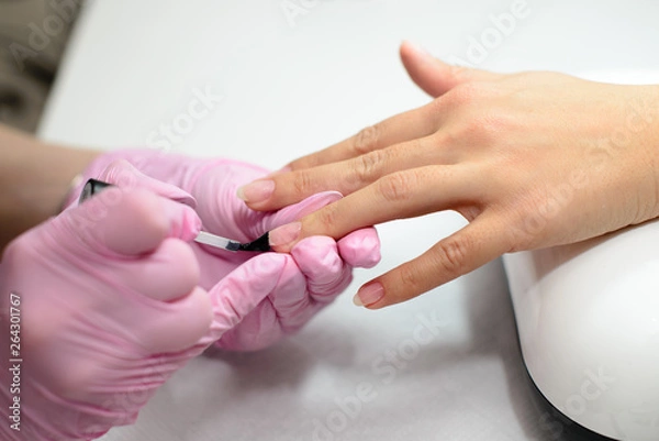 Fototapeta Closeup females hands getting manicure treatment from woman using small brush in salon environment, pink towel surface, blurry background products.
