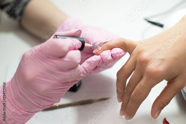 Fototapeta Closeup females hands getting manicure treatment from woman using small brush in salon environment, pink towel surface, blurry background products.
