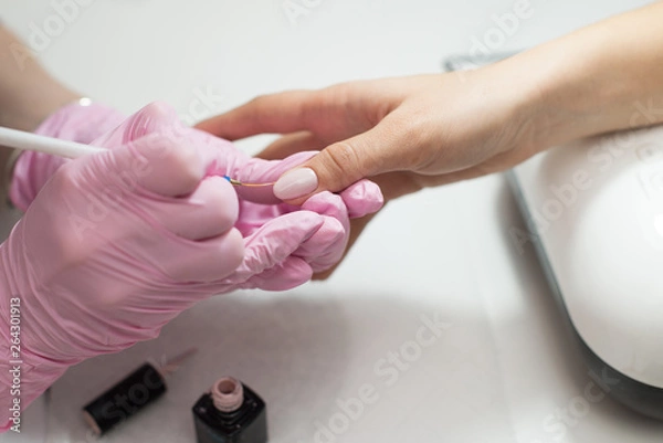 Fototapeta Closeup females hands getting manicure treatment from woman using small brush in salon environment, pink towel surface, blurry background products.