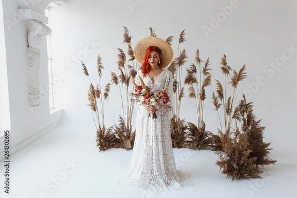 Fototapeta Wedding content - Close up Portrait young beautiful redhair girl in a hat in a studio on a white background with decorations. Copy space