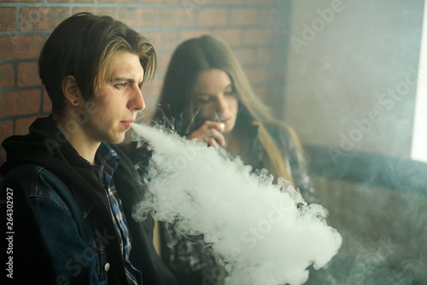 Fototapeta Vape teenagers. Young cute girl in sunglasses and young handsome guy smoke an electronic cigarettes in the vape bar. Bad habit that is harmful to health. Vaping activity.