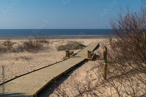 Fototapeta New wooden road leading from the beach dune forest with pines and white sent to the Baltic Sea gulf - Vecaki, Latvia