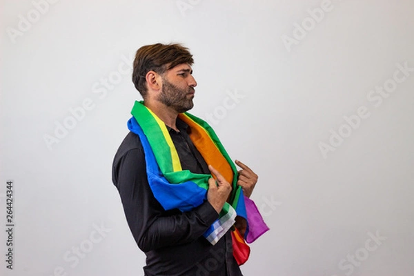 Fototapeta Portrait of handsome young man with gay pride movement LGBT Rainbow flag and brown hair showing nice face, facing forwards and looking at the side. Isolated on white background.