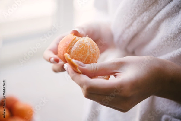 Obraz Woman cleans the tangerine with hands close up