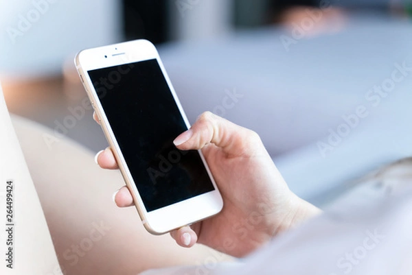 Obraz girl sitting comfortably on the couch uses a smartphone to surf the internet and chat