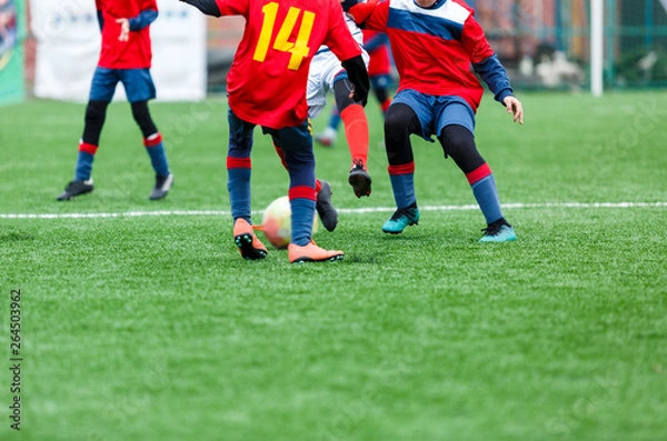 Fototapeta Boys kick soccer ball. Footballers run after the ball on green grass. Kids in white and red shirts dribbling, improve skills. Training, football, hobby, active lifestyle