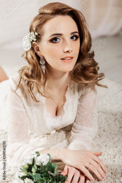 Fototapeta Beautiful girl with blond hair in a bright room is lying on the floor. Bride lying looking at the camera and smiling