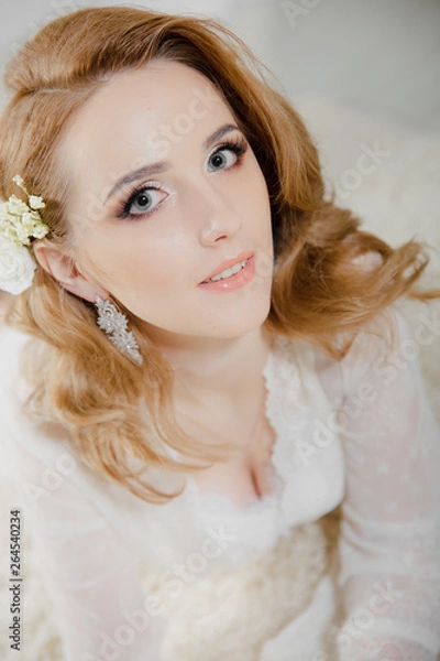 Fototapeta Beautiful girl with blond hair in a bright room is lying on the floor. Bride lying looking at the camera and smiling