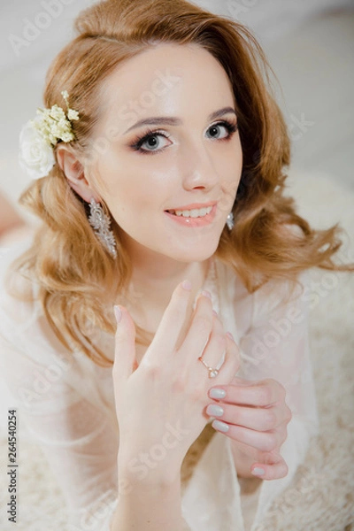 Fototapeta Beautiful girl with blond hair in a bright room is lying on the floor. Bride lying looking at the camera and smiling