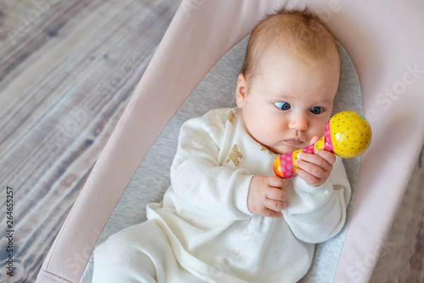 Fototapeta Adorable baby girl having fun in bouncer. Toddler playing with colorful rattle toy. Activities for infants