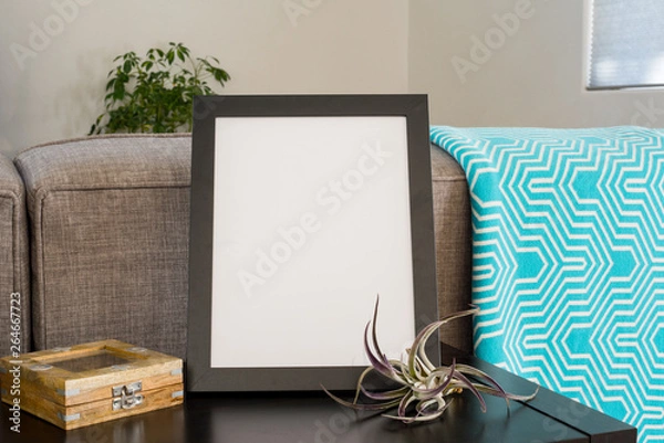 Fototapeta Black 8x10 frame on a livingroom  table top with a teal blanket airplant and puzzle box.