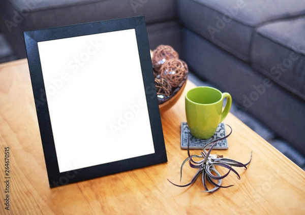Fototapeta Blank picture frame on a coffee table with a green mug and decor in the living room.