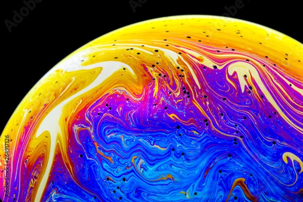 Fototapeta Multicolored rainbow colors of a single soap bubble that looks like a fantasy planet isolated against a black background 