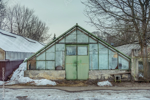 Fototapeta Old greenhouse made of glass with a triangular roof. Cloudy day in early spring.