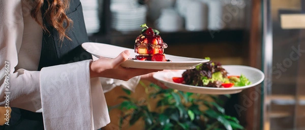 Fototapeta Waiter serving in motion on duty in restaurant. The waiter carries dishes