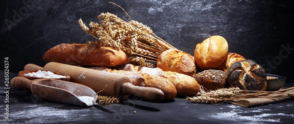 Fototapeta Assortment of baked bread and bread rolls on rustic black bakery table background