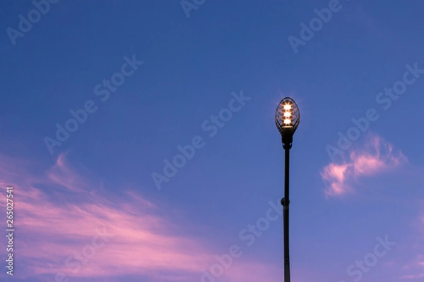 Fototapeta city street lantern illumination on evening sunset blue sky background with clouds in pink sun lighting, copy space