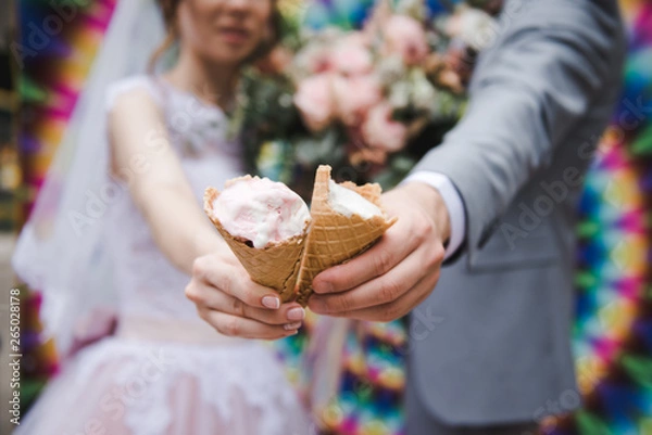 Obraz The bride and groom are eating ice cream together on a bright wall background. Funny newlyweds eat ice-cream. Happy Wedding Day