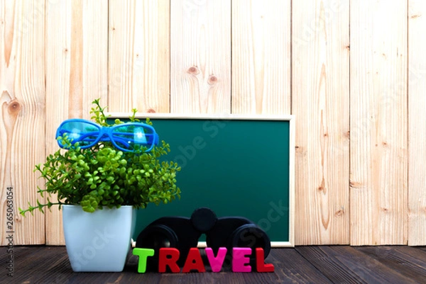Fototapeta TRAVEL letters text and notebook paper, alarm clock and little decoration tree in white vase on wooden background, travel vacation concept.