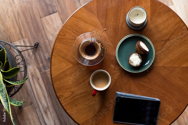Fototapeta A top down shot of modern living room coffee table with a coffee cup, book, tablet, and a muffin on it.