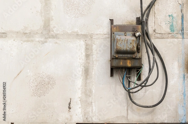 Fototapeta old rusty unkempt electric shield with a switch on the wall of an industrial building made of concrete blocks with molten wires sticking out of it