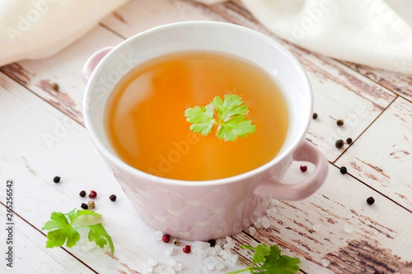 Fototapeta Cooked hot bone broth with spices and fresh herbs. Medical dietary broth and superfood. For ketogenic diet and paleo diet. Serve on an individual plate on a wooden background and with a white napkin.