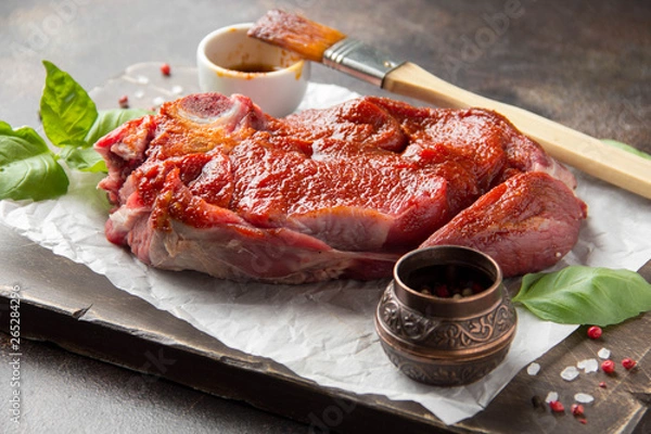Obraz Raw beef on bone, cooking steak with spices, barbecue marinade, red sauce. Traditional food, uncooked meat on Board