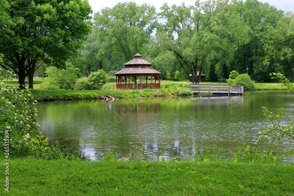 Fototapeta Midwest nature background with city park view. Beautiful late spring landscape with trees around the pond and wooden gazebo in a city park. Lakeview park, Middleton, Madison area, WI, USA.
