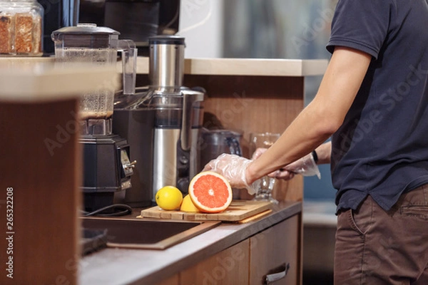 Fototapeta Side view young male bartender makes fruit juice standing behind the bar in the evening bar. Soft drink concept
