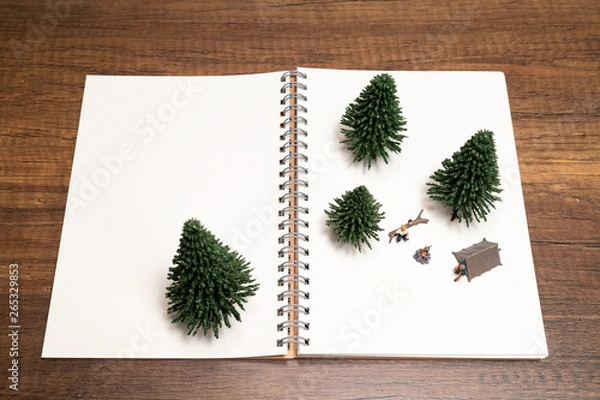 Fototapeta Two miniature camping with pine tree on white blank notebook