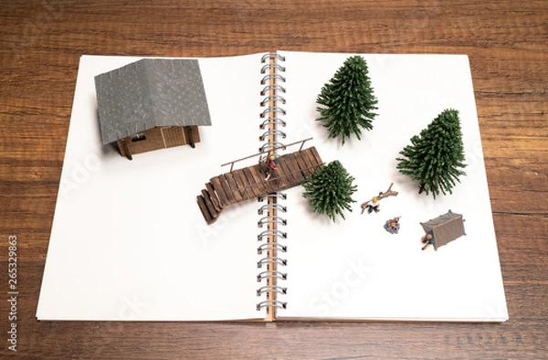 Fototapeta Two miniatures camping with Pine tree, Bridge and House on white blank notebook